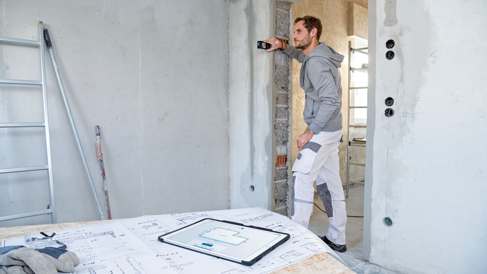 A craftsman measures with a Bosch tool in a construction site.