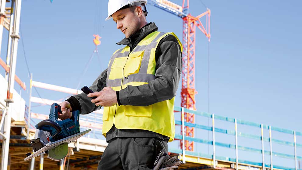 A man in a safety vest holds a Bosch Professional circular saw on a construction site.