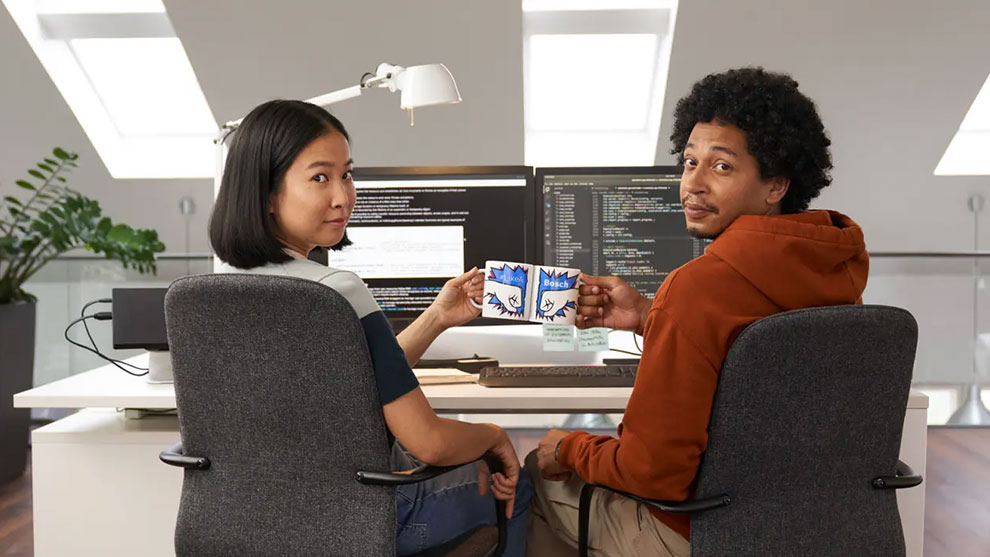 Two people are sitting at the desk holding coffee cups from Bosch.