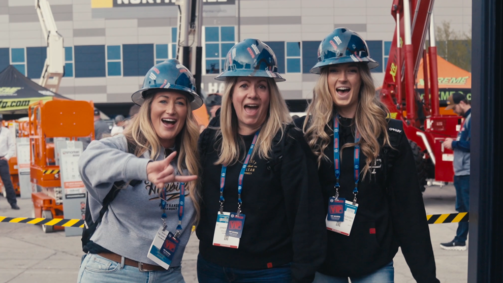 Trois femmes en casques bleus rient et posent devant un chantier.