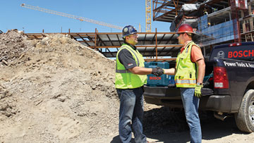 Two men in safety vests shake hands at a construction site.