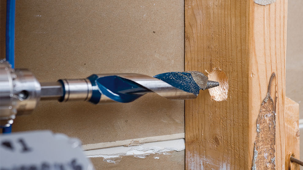 Une perceuse bleue Bosch Professional perce un morceau de bois.