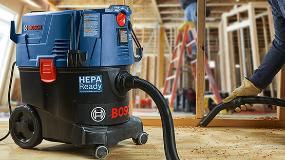 A blue Bosch Professional vacuum cleaner stands on a wooden floor.