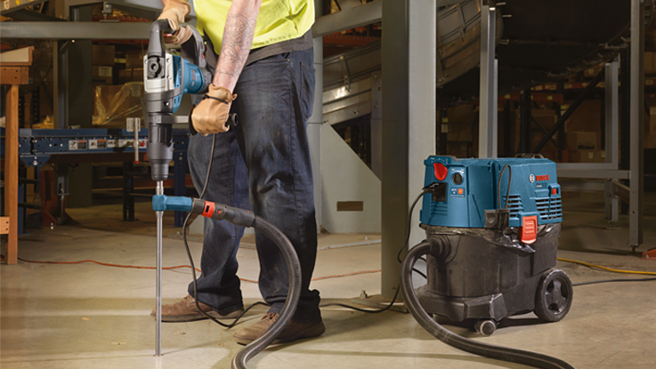 A worker with a Bosch Professional rotary hammer stands next to a vacuum cleaner.