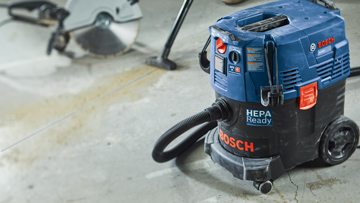 Una aspiradora azul Bosch Professional está sobre un suelo de concreto.