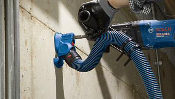 Se está utilizando un extractor de polvo de perforación azul Bosch Professional en una pared.