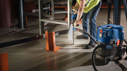 Un trabajador con chaleco amarillo está operando una aspiradora azul Bosch.