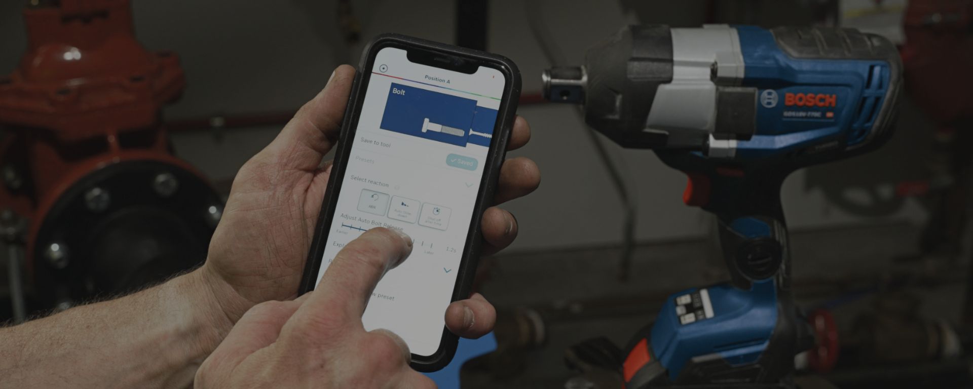 A person holds a smartphone with a Bosch Professional app, while a blue battery impact wrench stands next to it.