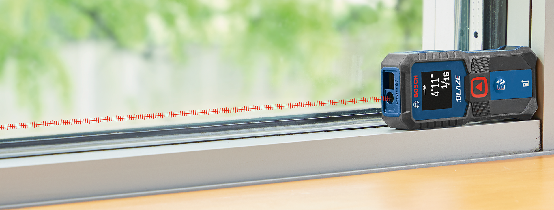 A blue laser distance meter is lying on a windowsill, next to a red laser line.