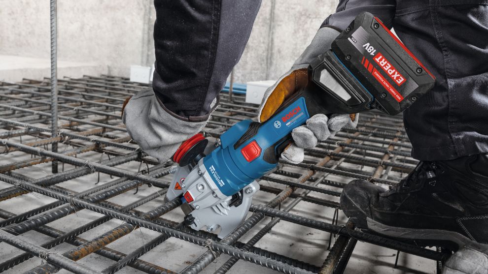 Una cortadora a batería Bosch Professional azul es sostenida por una persona sobre una rejilla de acero.