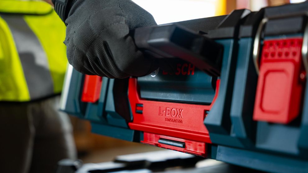 Une main dans un gant noir saisit une boîte à outils rouge L-BOXX de Bosch Professional.