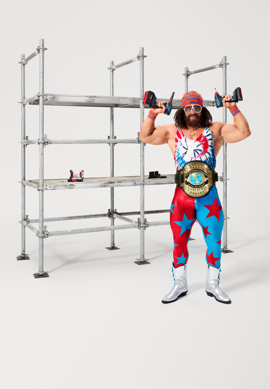 Un hombre musculoso con ropa colorida sostiene dos taladros.