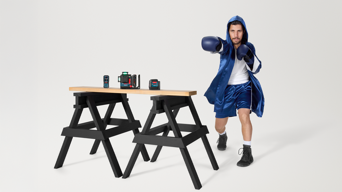 A man in a blue boxing suit strikes towards a wooden table on black supports.