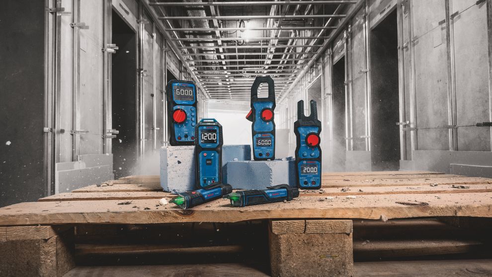 Six blue Bosch Professional measuring devices are placed on a wooden pallet. In the background, construction site walls are visible.