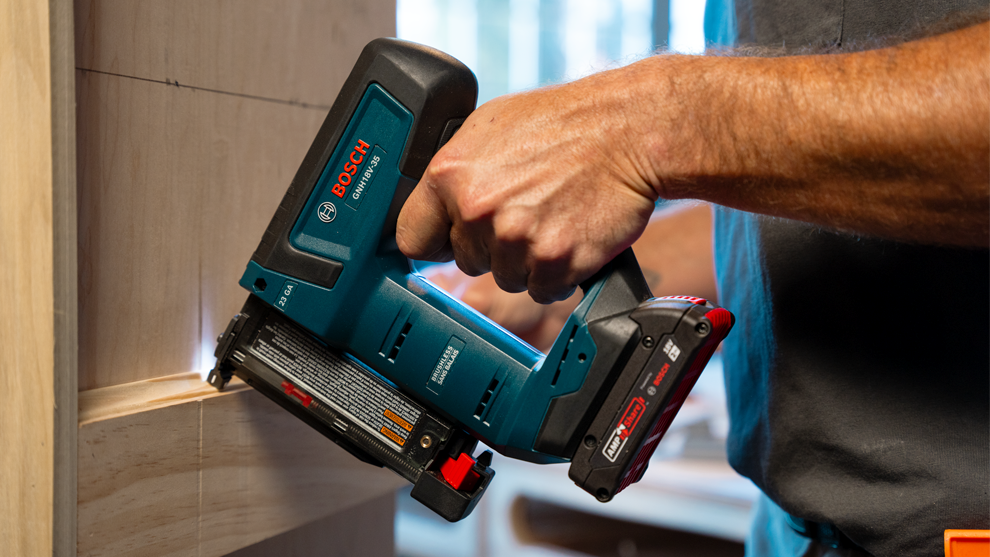 A person is using a blue Bosch Professional battery nailer on wood.