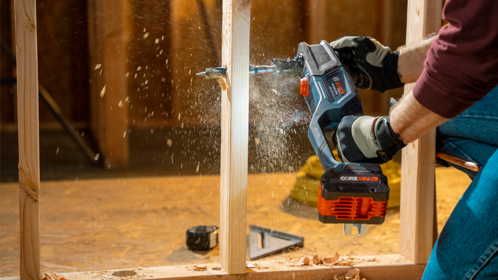 A Bosch Professional cordless tool is drilling into wood, shavings are flying around.