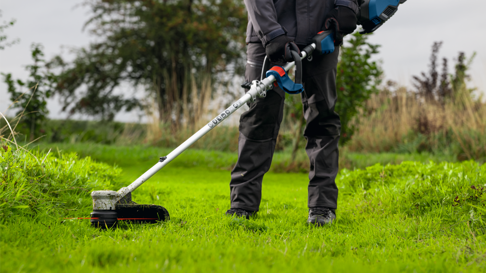 A person in black work clothes is mowing the green grass in a garden with a lawn mower.