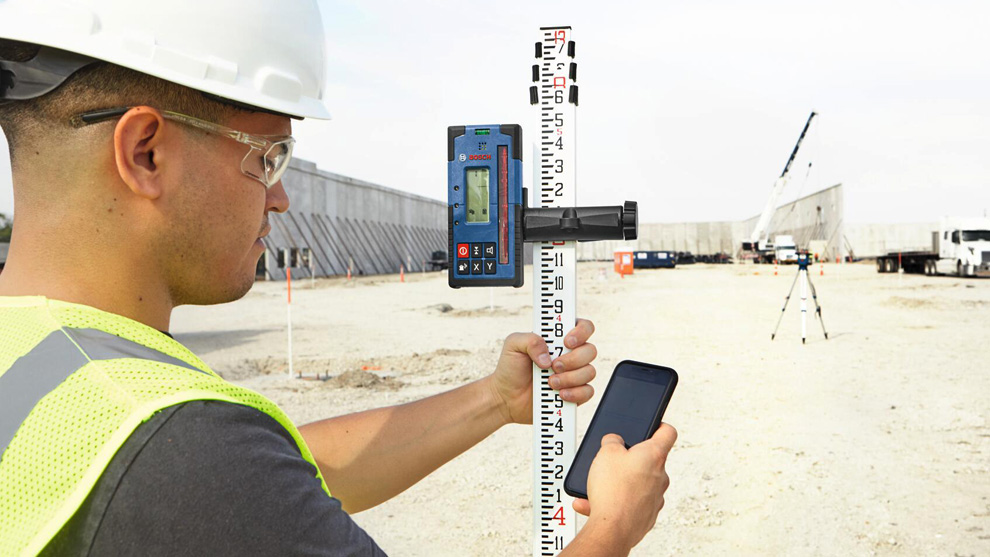 Un hombre con casco mide con un dispositivo láser Bosch en un sitio de construcción.
