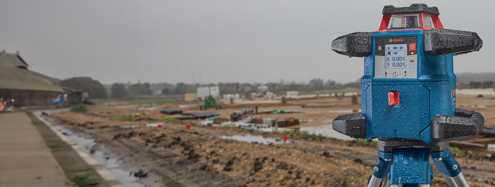 A blue laser level stands on a tripod, surrounded by construction materials.