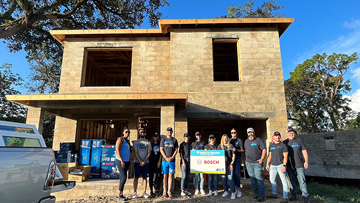 A group of people stands in front of an unfinished house with a Bosch sign.