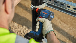 A man with gloves is using a blue Bosch Professional cordless drill.