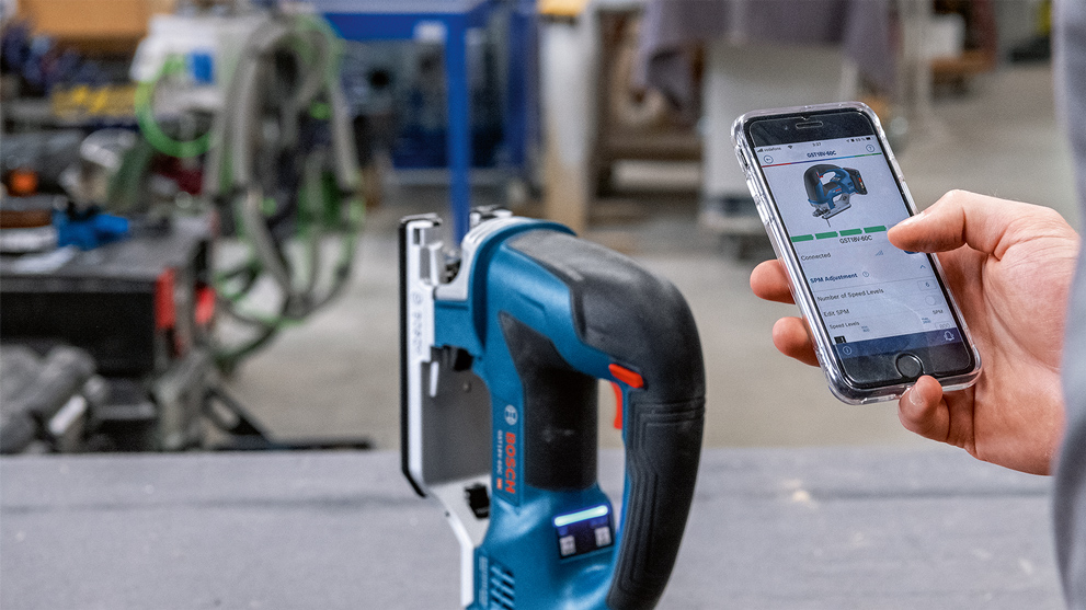 A Bosch Professional cordless jigsaw is on a table, hand with a phone.