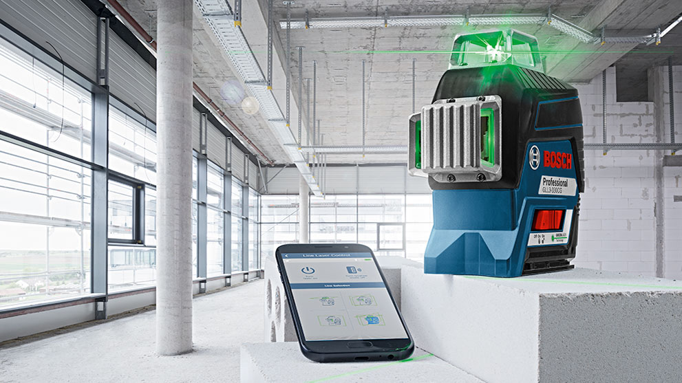 Bosch Professional laser device stands on a white block next to a smartphone.