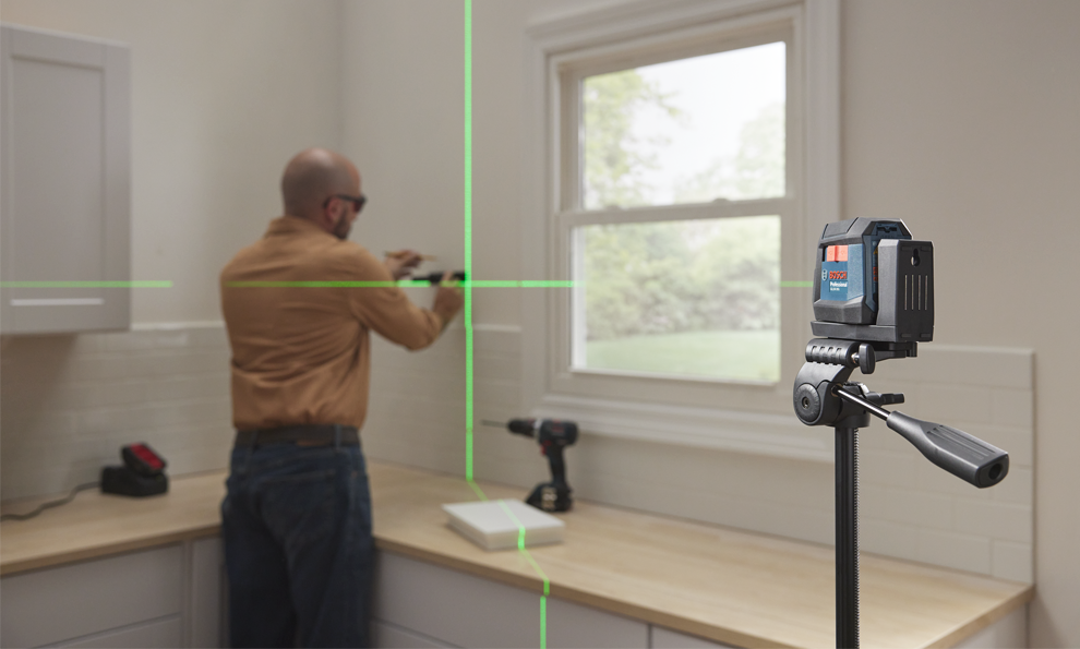 A craftsman in a bright room is installing a wall mount while a laser device projects.
