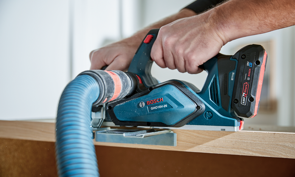 A hand holds a Bosch electric planer working on a piece of wood.